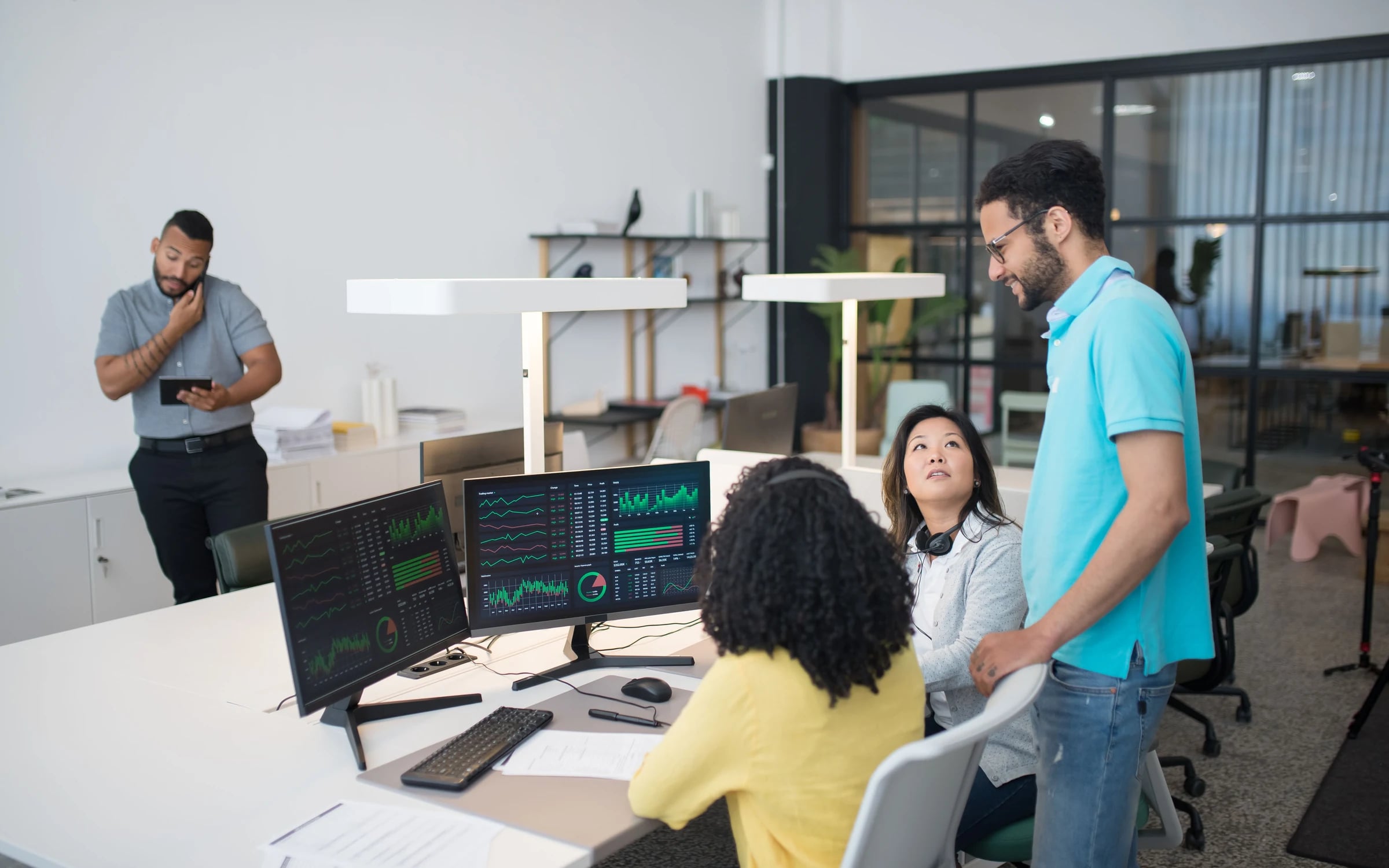 Colleagues around a workstation with two monitors showing live system activity dashboards