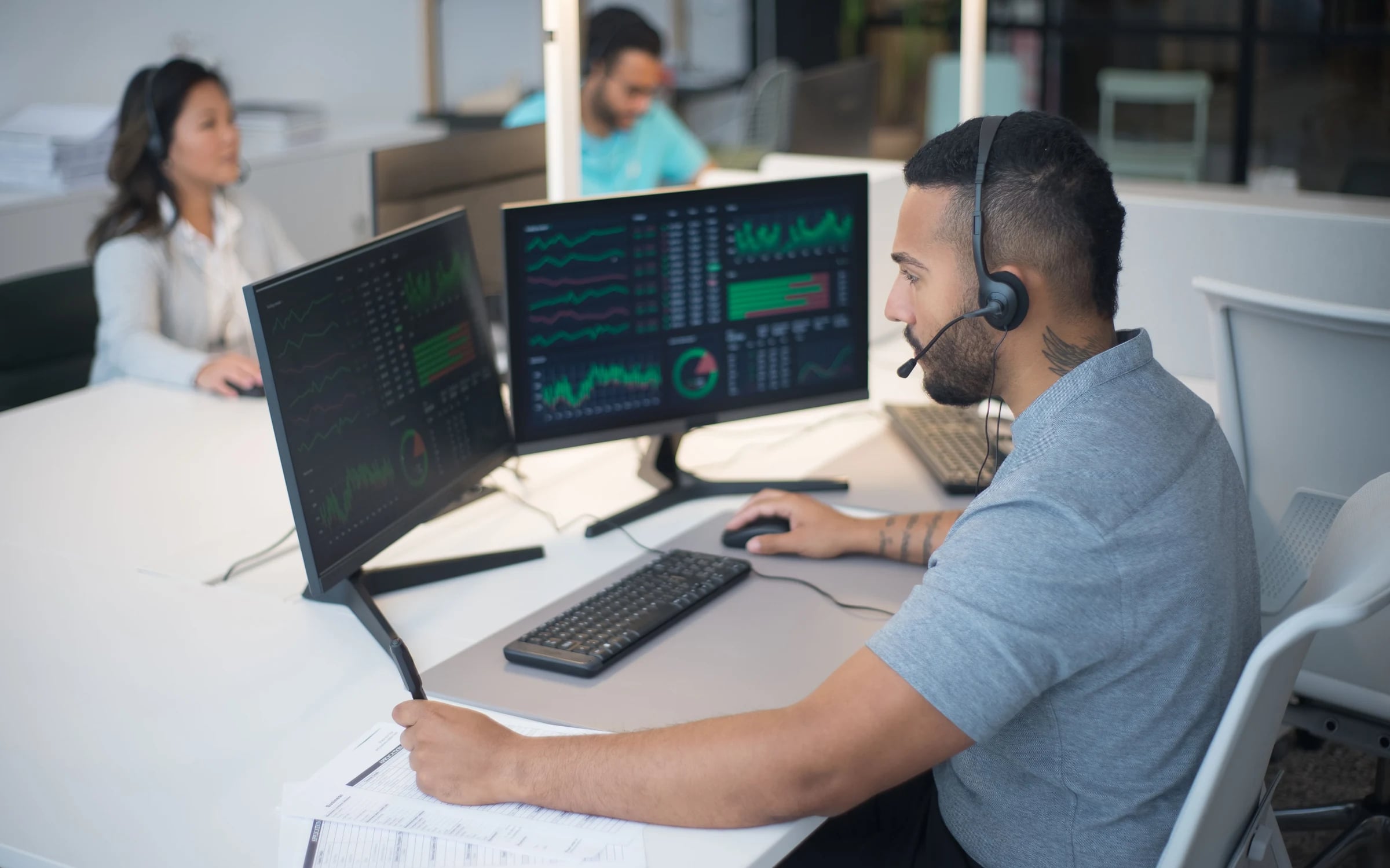A support engineer with a headset watching system health dashboards on two monitors
