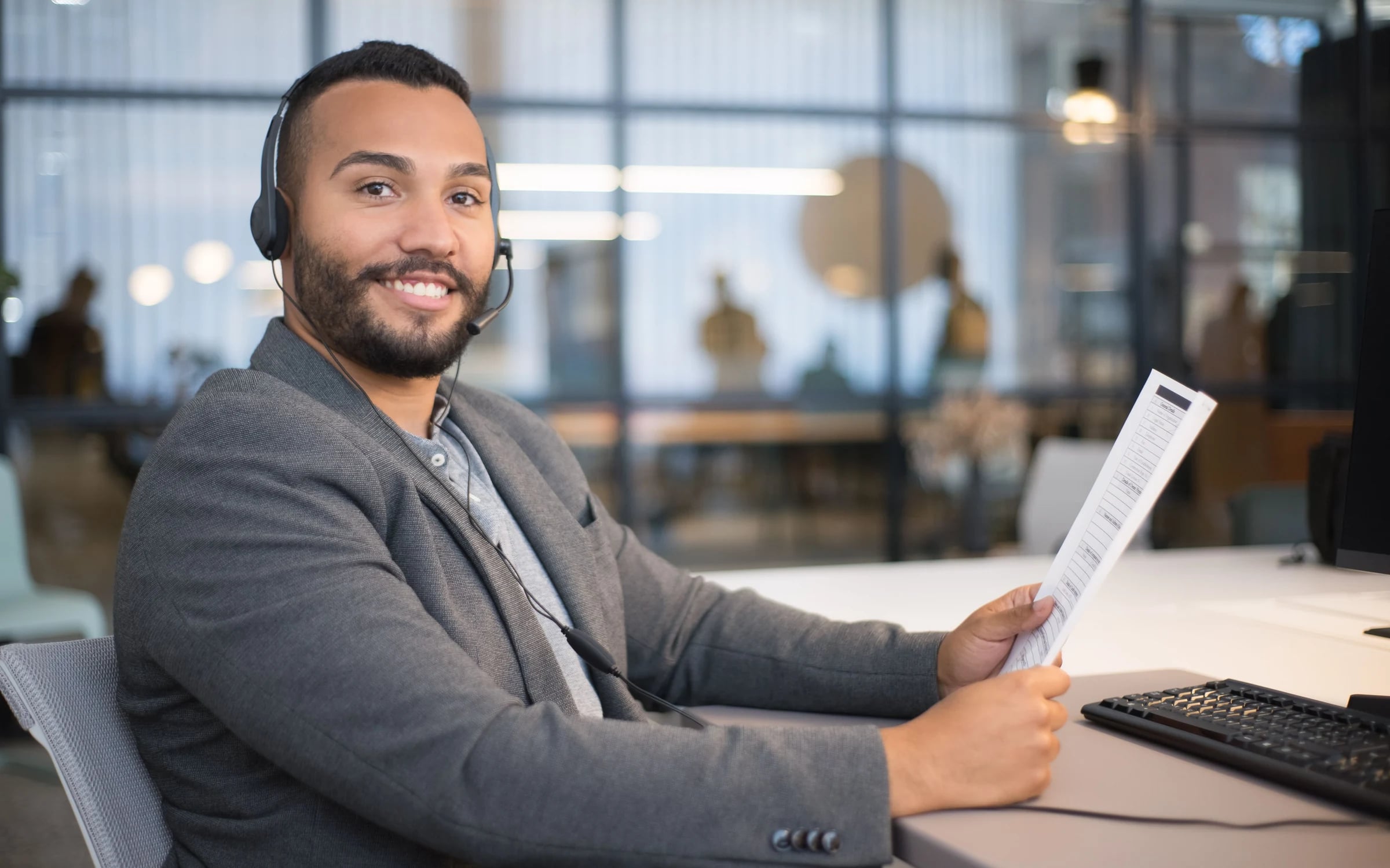 Smiling recruiter in a headset reviewing a printed form at a desk in a glass-walled office