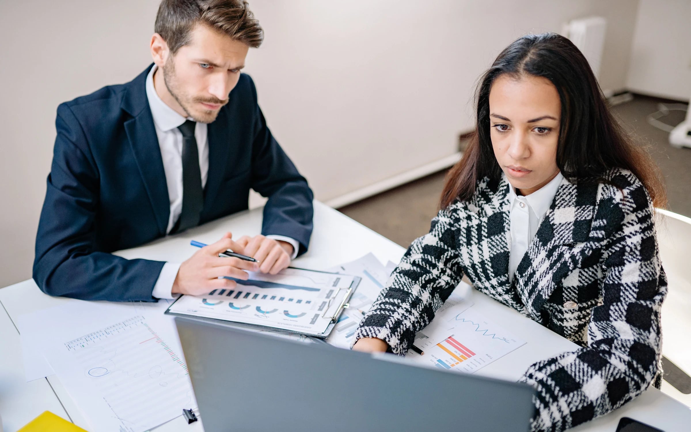 Two colleagues reviewing workforce charts on paper and a laptop at a desk