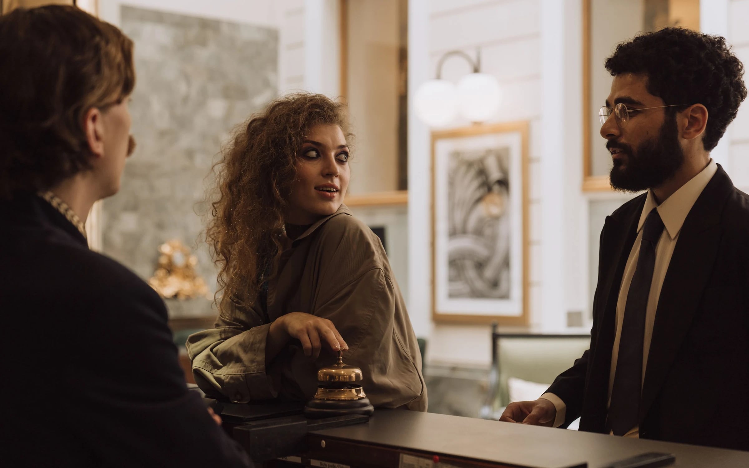 Guests at a hotel front desk talking with a staff member beside a service bell