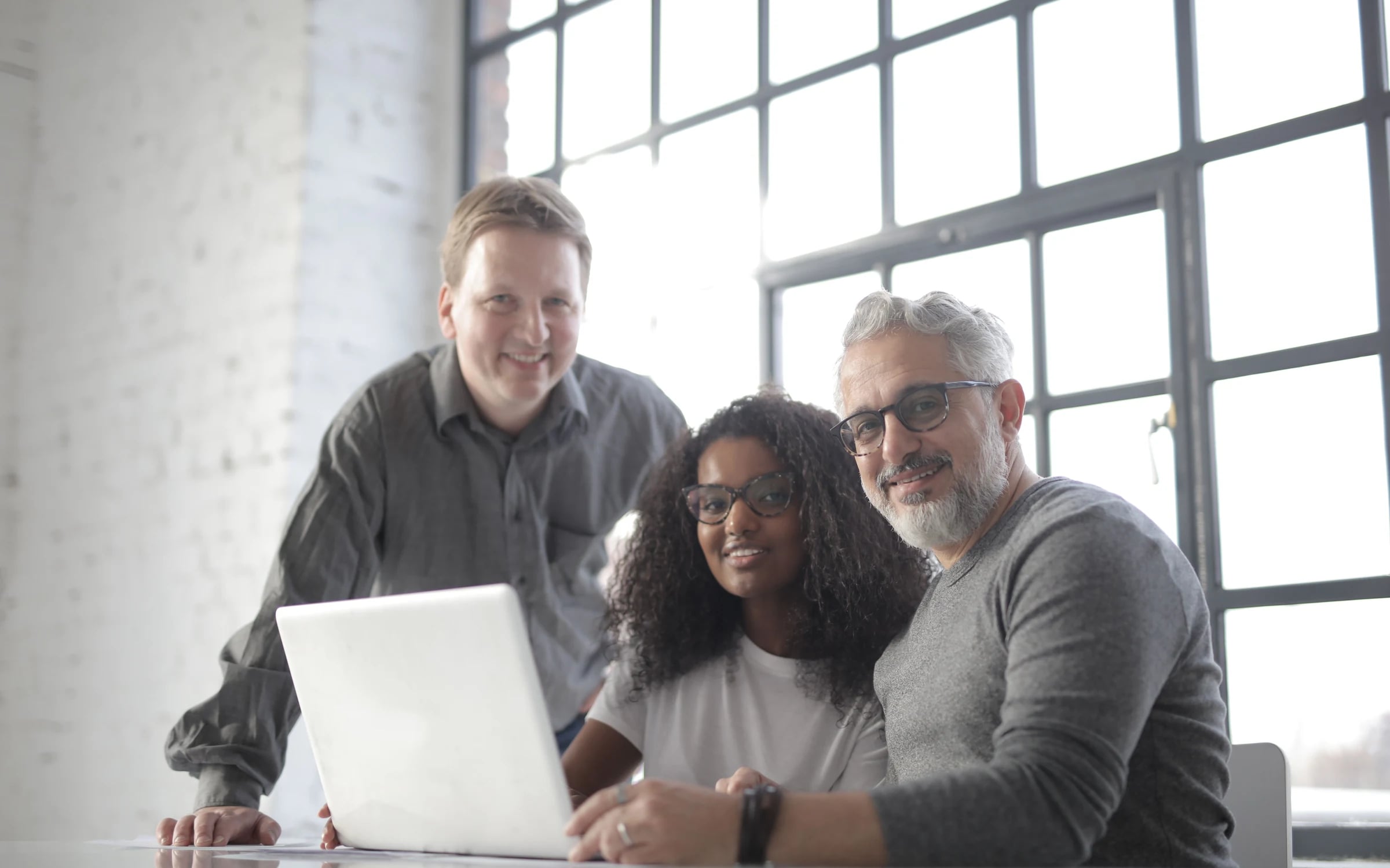 Three colleagues smiling together over a laptop at a shared desk