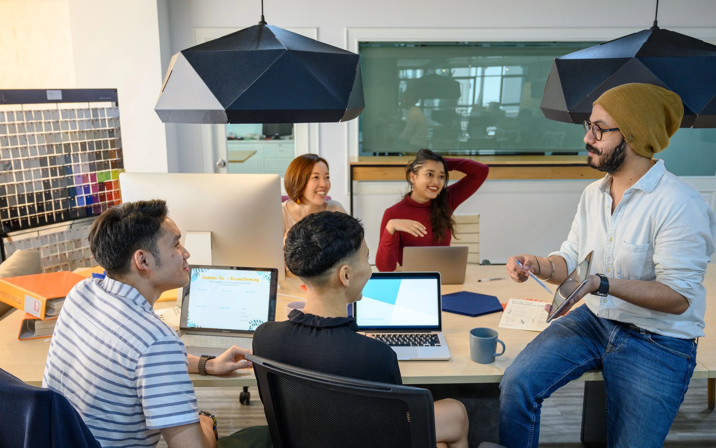 A project team meeting around a table with laptops and a tablet in a creative office