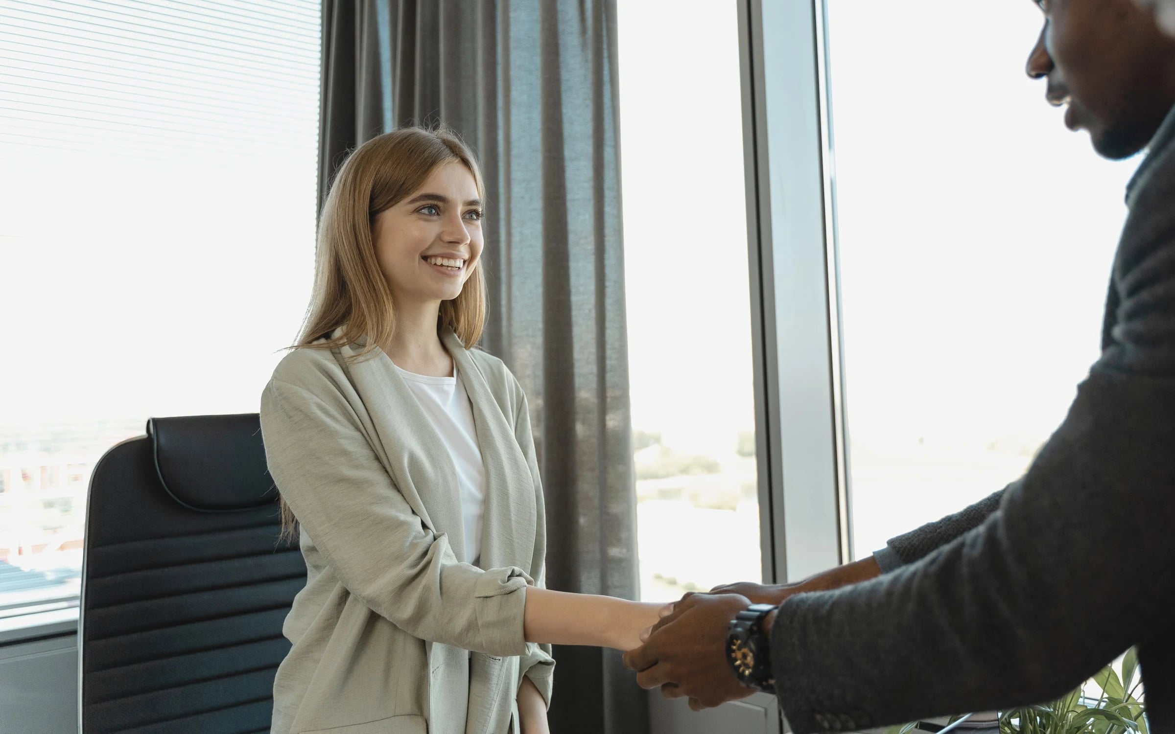 A smiling candidate shaking hands with an interviewer in an office meeting room